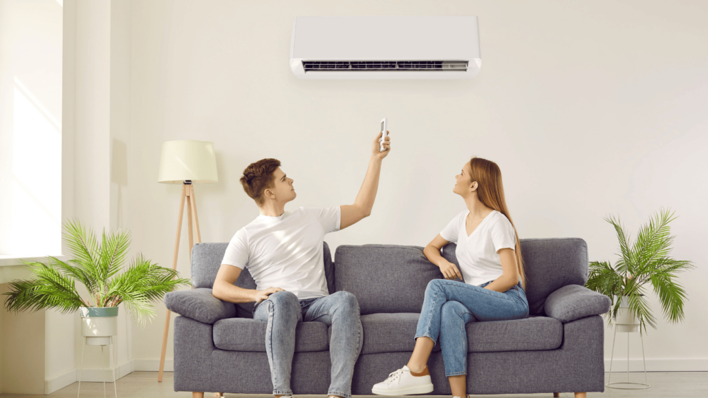 A young couple sitting on a sofa and the man is switching on he ac